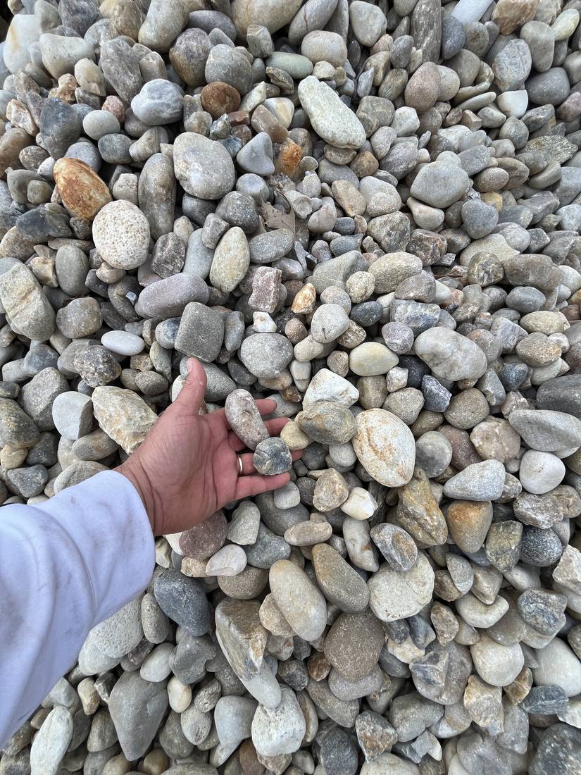 A hand holding river rock over a fresh load of stone