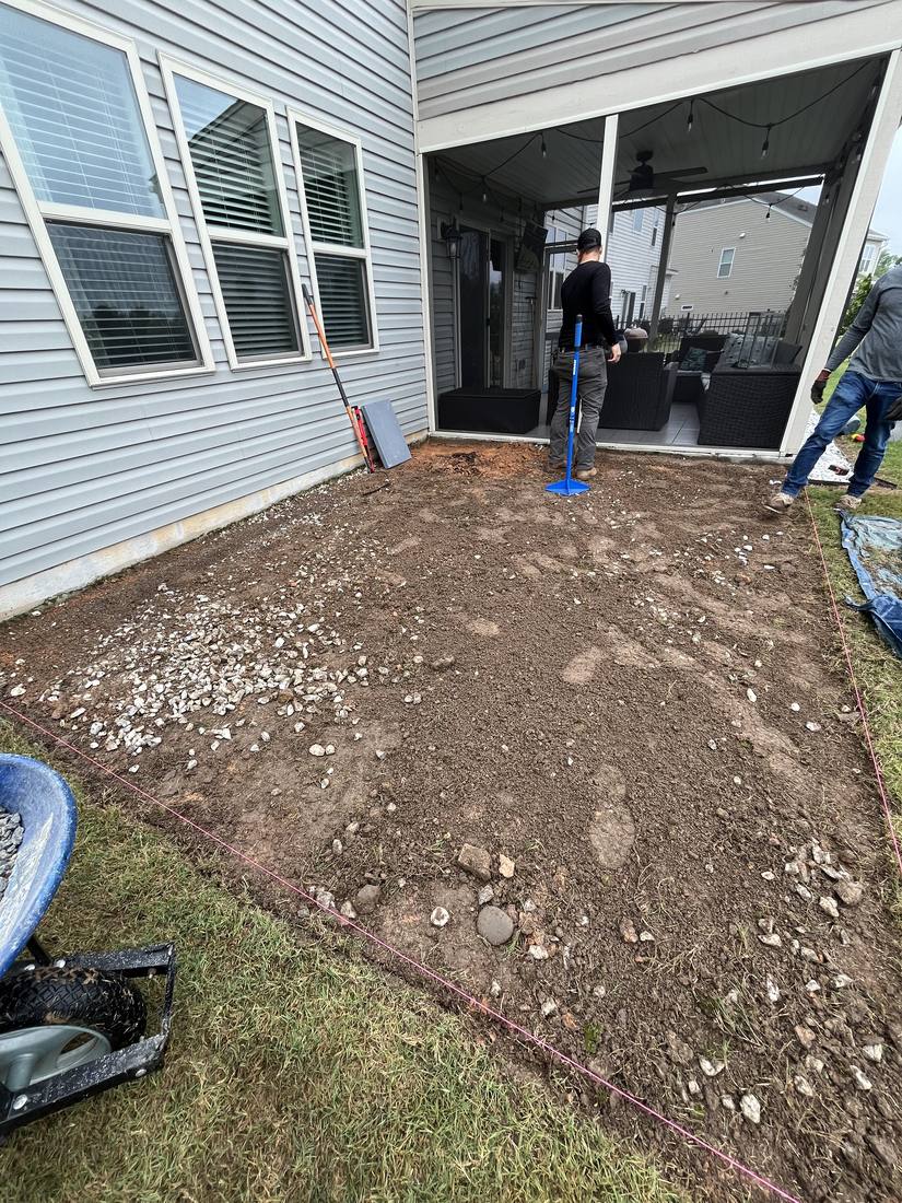 Bare graded dirt beside a screened porch, string lines set for a patio