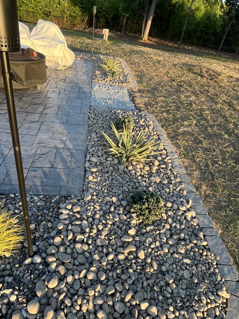 Dark river stone bed beside a flagstone patio with yucca plants