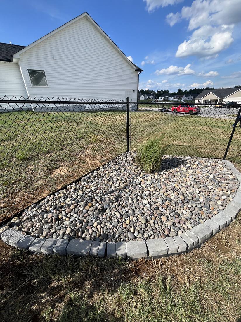 River rock corner bed with paver block border along a fence